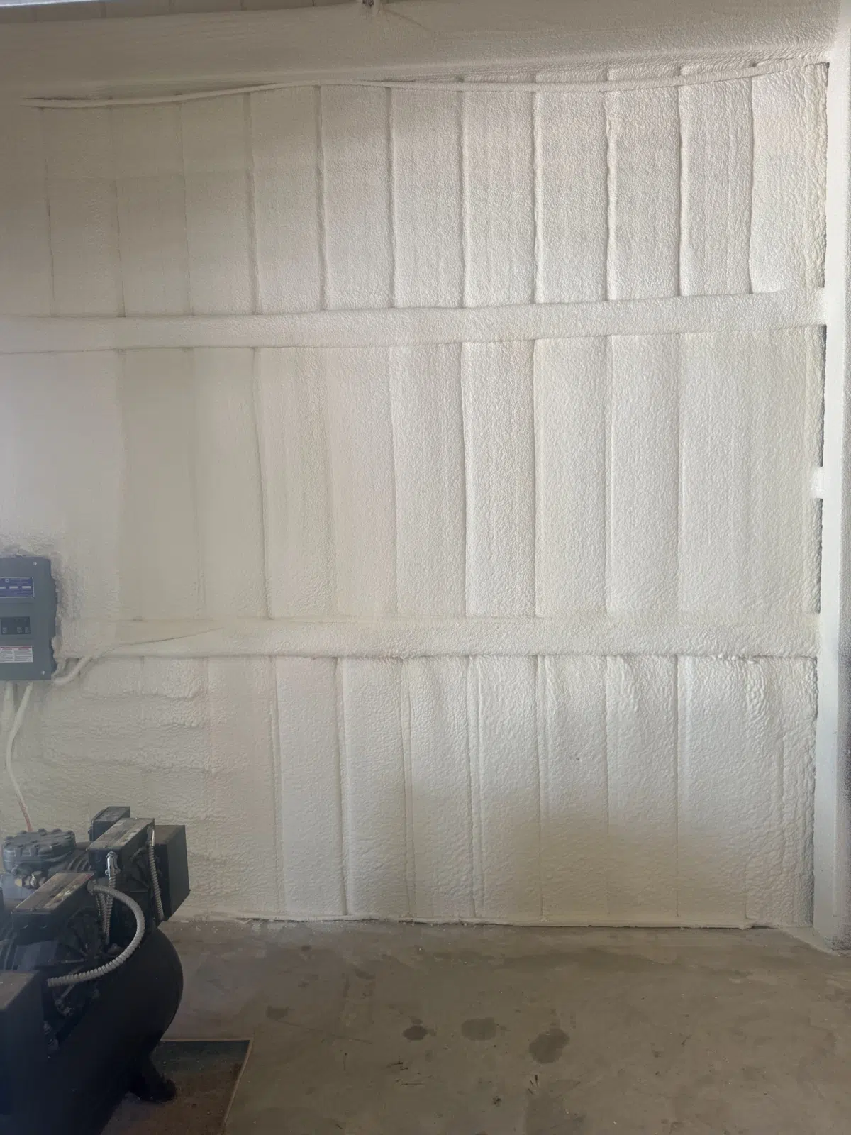 White spray foam insulation covering a shop wall with air compressor — Missouri Foam Solutions in Thayer