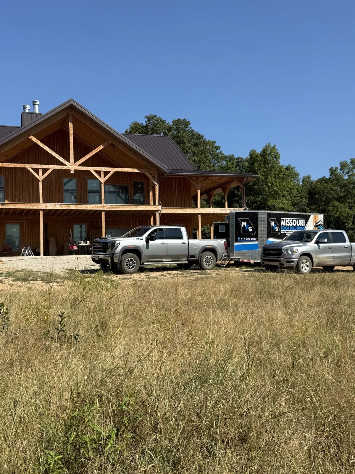 Work trucks and trailer parked outside a new timber-frame home — Missouri Foam Solutions in Thayer